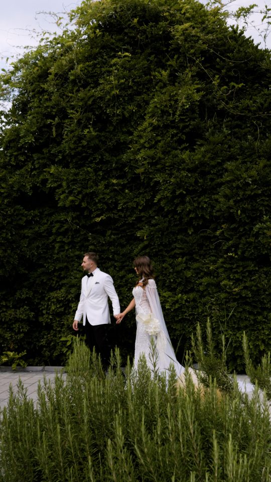 Bride and groom walking hand in hand beside a green wall